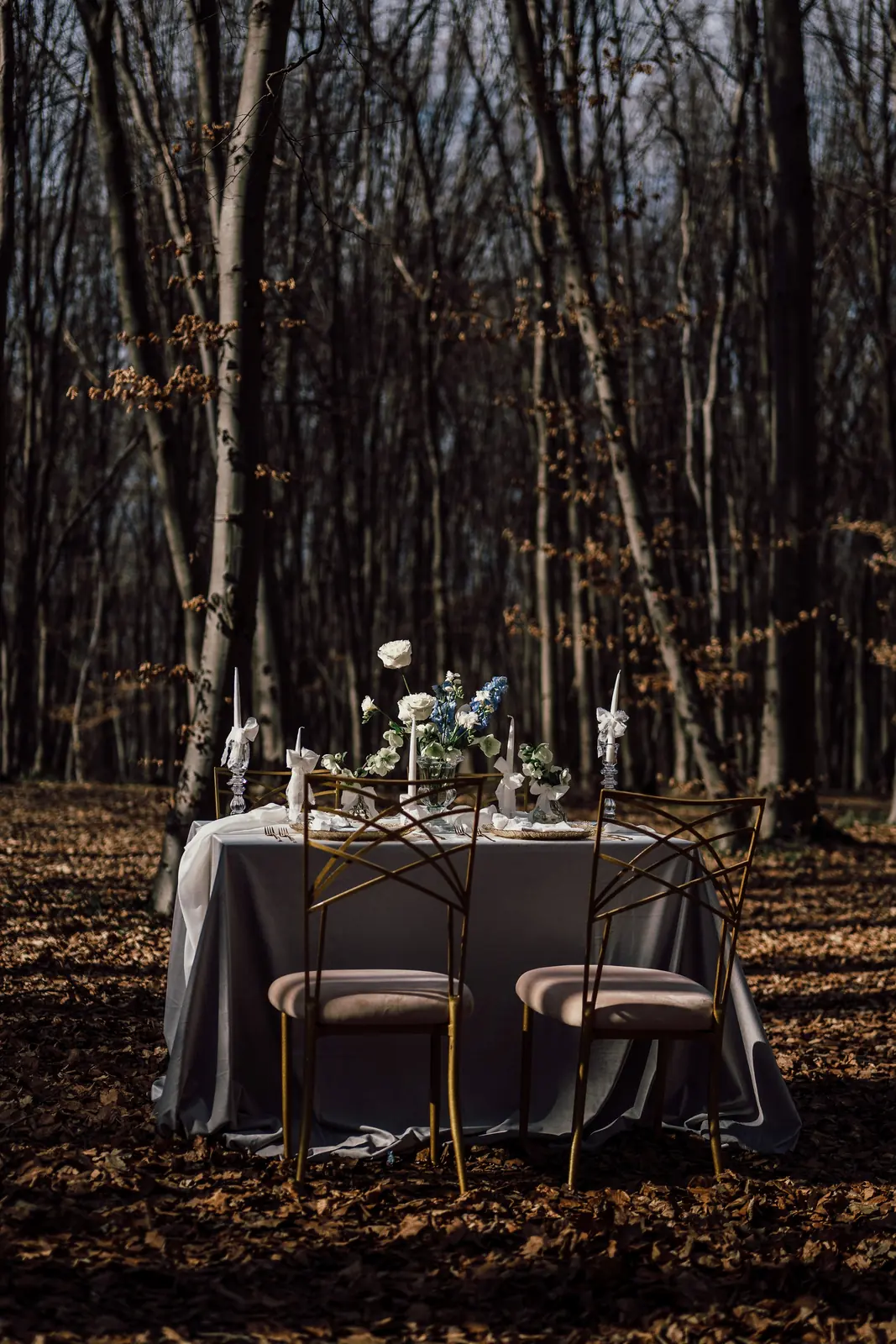 Cină romantică amenajată în pădure, cu masă rotundă și lumânări